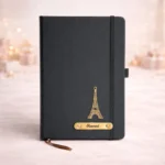 Black stainless steel water bottle with custom name engraving standing next to a box of gold-wrapped chocolates and a cute plush teddy.