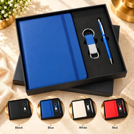 Premium personalized corporate gift set featuring a blue hardcover notebook with elastic closure, matching metallic finish pen and customized keychain, presented in an elegant black gift box. Available in black, blue, white and red.