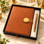 Premium brown executive diary and matching metal pen corporate gift set featuring a textured leatherette notebook with elegant round gold magnetic closure, brown stitching and matching gold-accented pen, presented in a luxury black gift box.